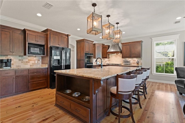 kitchen featuring black appliances, light wood-type flooring, an island with sink, tasteful backsplash, and decorative light fixtures