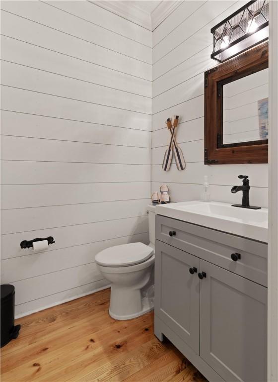 bathroom featuring hardwood / wood-style flooring, vanity, wood walls, and toilet