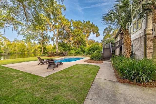 view of swimming pool featuring a patio area, a water view, and a yard