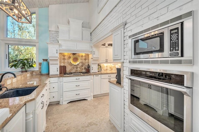 kitchen with light stone countertops, stainless steel appliances, sink, pendant lighting, and white cabinets