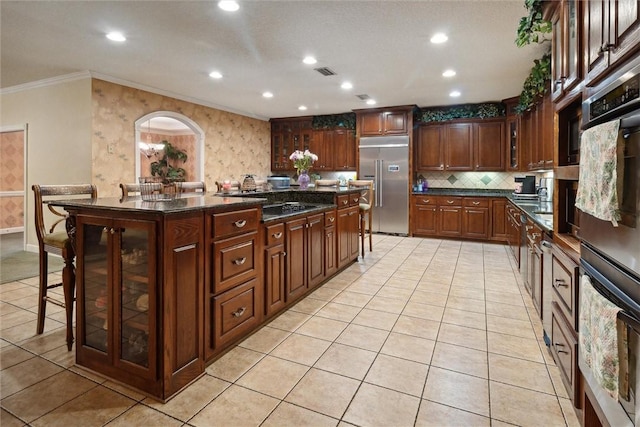 kitchen featuring light tile patterned floors, built in fridge, crown molding, a breakfast bar area, and a kitchen island