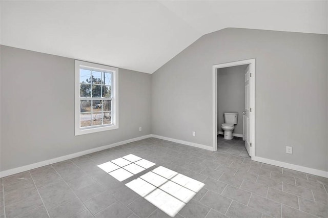 unfurnished bedroom with ensuite bath, lofted ceiling, and light tile patterned floors