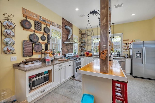 kitchen featuring visible vents, a kitchen bar, stainless steel appliances, wall chimney exhaust hood, and white cabinetry