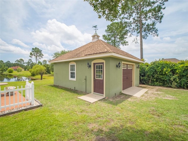 rear view of house featuring a garage, a water view, a yard, and an outbuilding