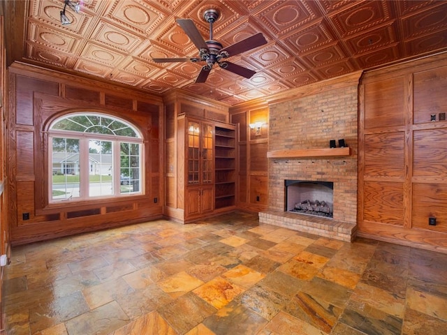 unfurnished living room with a fireplace, ceiling fan, and wood walls