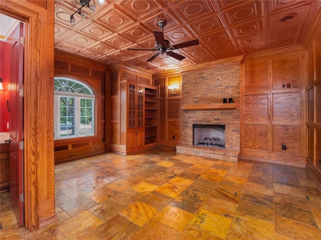 unfurnished living room with ceiling fan, a fireplace, and wood walls