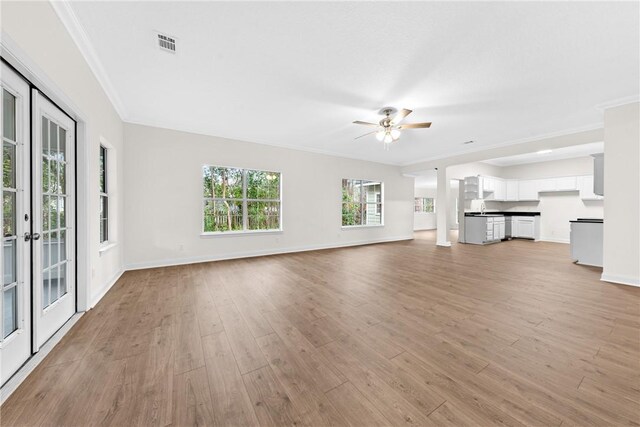 unfurnished living room with ceiling fan, light hardwood / wood-style floors, crown molding, and french doors