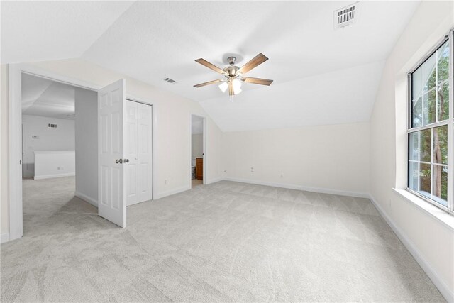 interior space featuring ceiling fan, a healthy amount of sunlight, light carpet, and vaulted ceiling