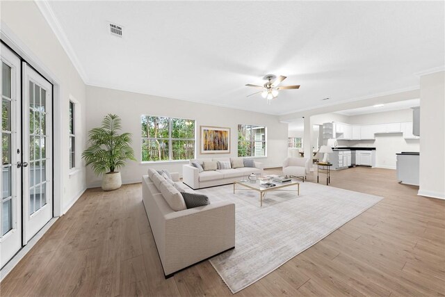 living room with french doors, light wood-type flooring, ceiling fan, and ornamental molding