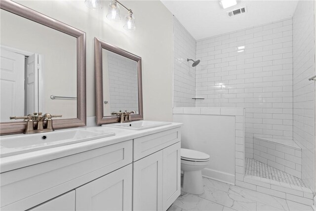 bathroom with a tile shower, vanity, and toilet