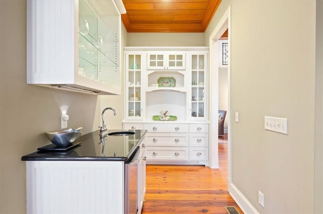 kitchen featuring light wood-style flooring, a sink, dark countertops, white cabinetry, and wood ceiling