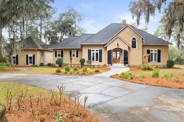 view of front facade with stucco siding, french doors, and a chimney