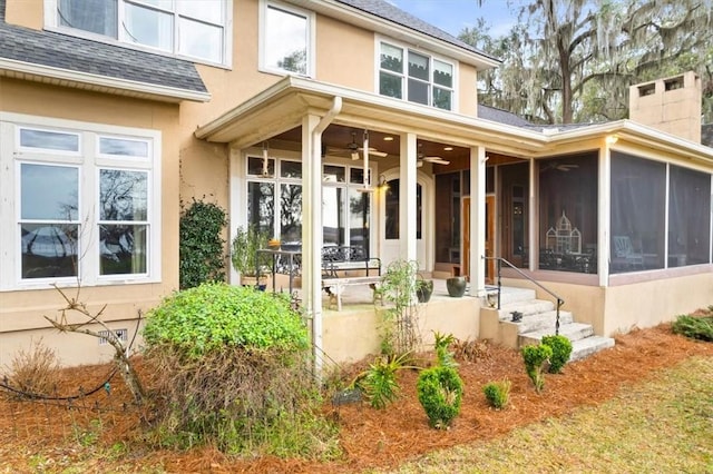 back of house featuring stucco siding, a ceiling fan, roof with shingles, a sunroom, and a chimney