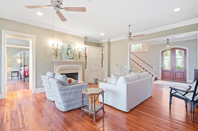 living area featuring stairway, baseboards, light wood-style floors, and ornamental molding