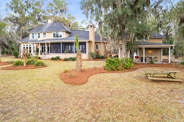 back of property featuring a yard, a patio area, a chimney, and a sunroom