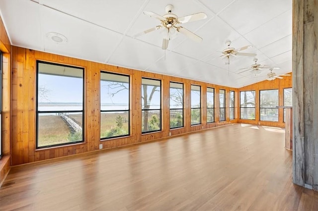 unfurnished sunroom with a water view, wooden walls, wood finished floors, and lofted ceiling