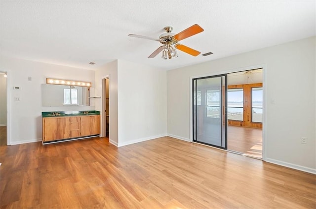 unfurnished living room with baseboards, light wood-style flooring, visible vents, and a ceiling fan