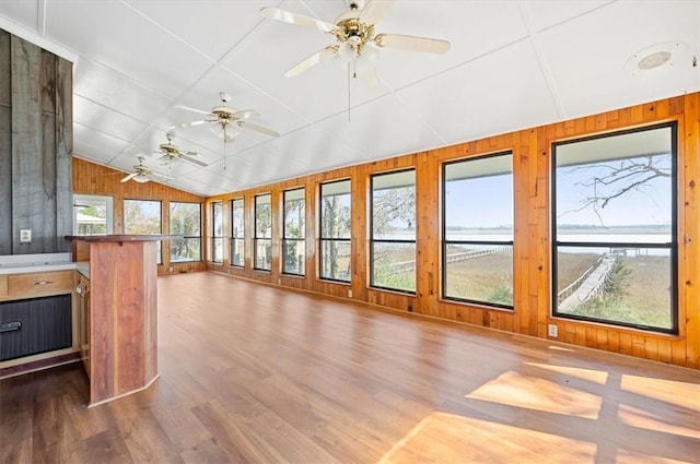 unfurnished sunroom featuring lofted ceiling, wooden walls, a water view, and wood finished floors