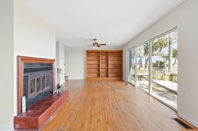 unfurnished living room featuring visible vents, built in shelves, light wood finished floors, a ceiling fan, and a tile fireplace