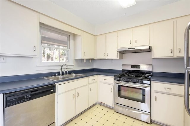 kitchen with under cabinet range hood, dark countertops, appliances with stainless steel finishes, and a sink
