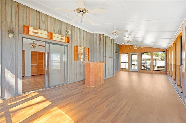 interior space featuring light wood-style flooring, visible vents, ceiling fan, wooden walls, and vaulted ceiling