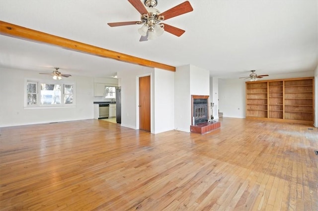 unfurnished living room featuring light wood-style flooring, a brick fireplace, beamed ceiling, and a ceiling fan