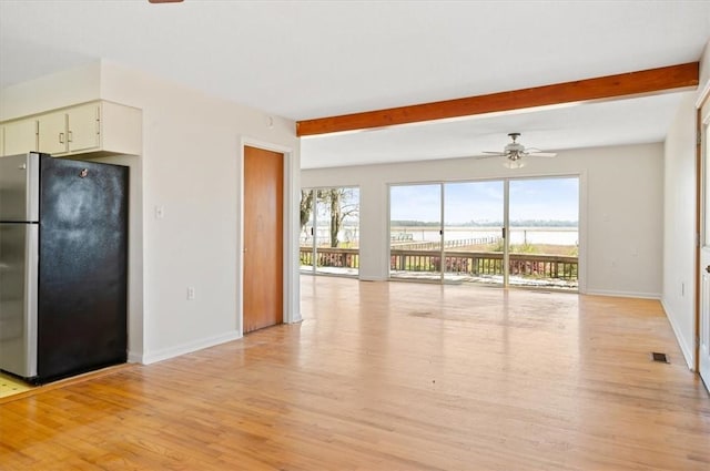 unfurnished living room featuring ceiling fan, a water view, baseboards, and light wood-style floors