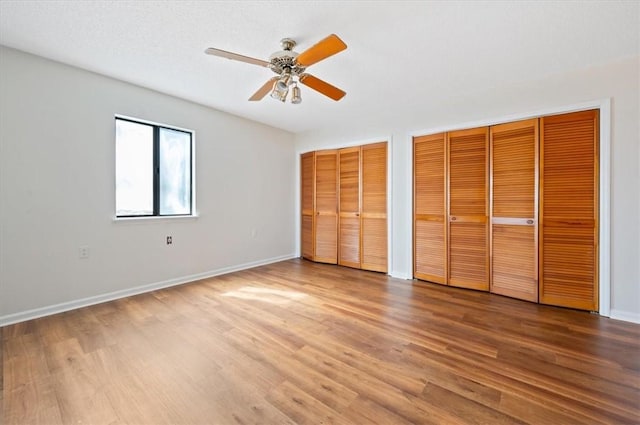 unfurnished bedroom with baseboards, two closets, a ceiling fan, and wood finished floors