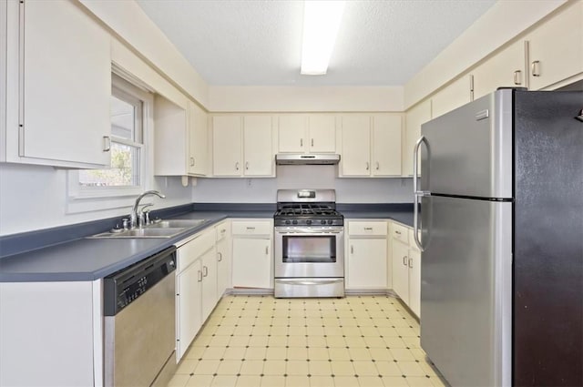 kitchen with dark countertops, a sink, appliances with stainless steel finishes, and under cabinet range hood