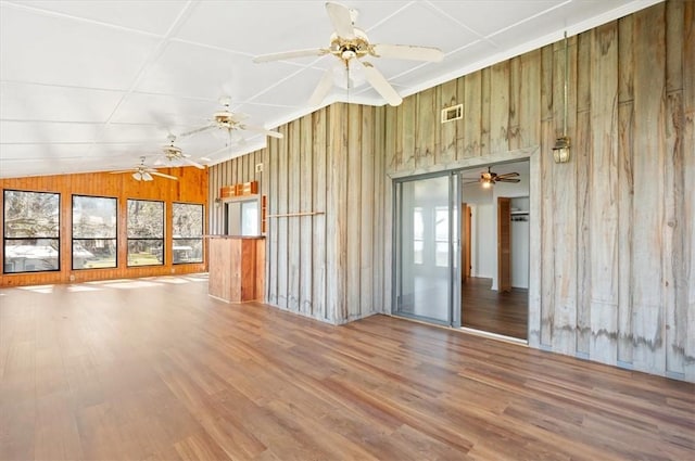 unfurnished living room featuring wood walls, plenty of natural light, visible vents, and wood finished floors