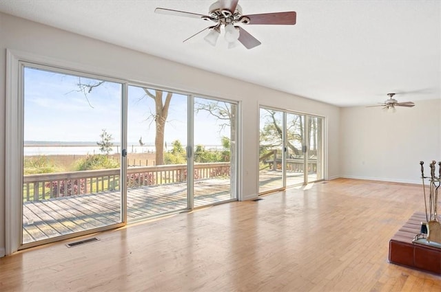 unfurnished living room with a ceiling fan, baseboards, a water view, and visible vents