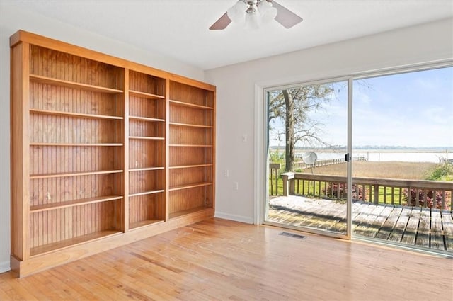 interior space with baseboards, ceiling fan, visible vents, a water view, and wood finished floors