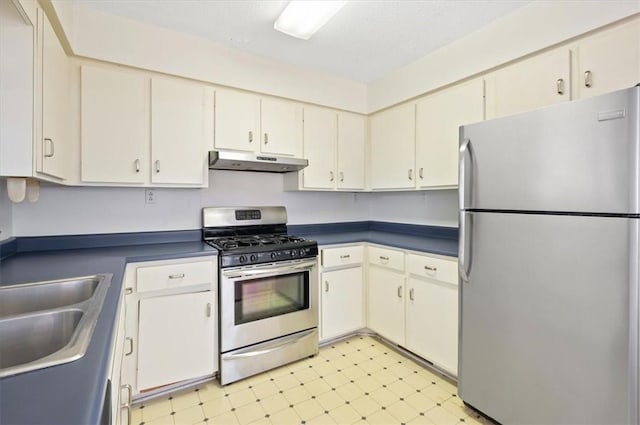 kitchen with a sink, dark countertops, light floors, under cabinet range hood, and appliances with stainless steel finishes