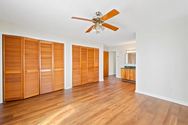 unfurnished bedroom featuring a ceiling fan, baseboards, light wood-type flooring, and multiple closets