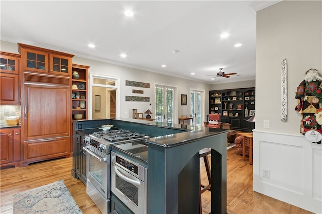 kitchen featuring ceiling fan, a kitchen breakfast bar, crown molding, high quality appliances, and light wood-type flooring