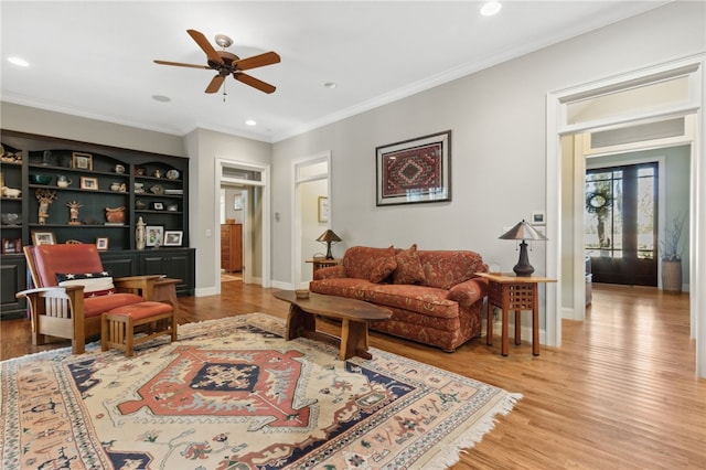 living room featuring ceiling fan, built in features, ornamental molding, and light wood-type flooring