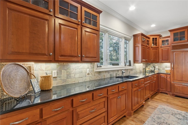 kitchen with crown molding, sink, dark stone countertops, light wood-type flooring, and tasteful backsplash