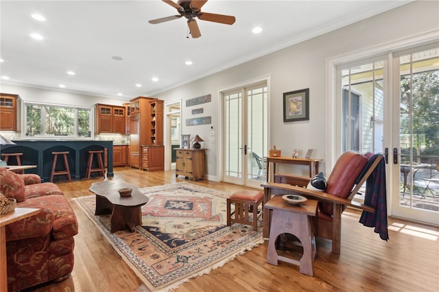 living room featuring light wood-type flooring, plenty of natural light, ceiling fan, and crown molding