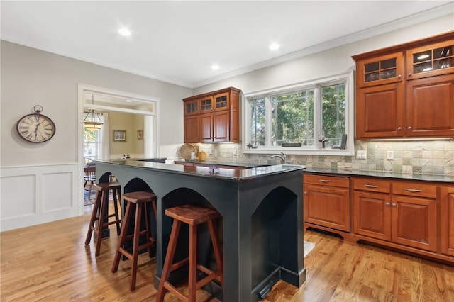 kitchen with a breakfast bar area, light hardwood / wood-style flooring, plenty of natural light, and ornamental molding