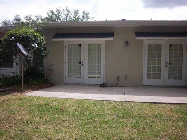 doorway to property with french doors, stucco siding, a patio, and a lawn