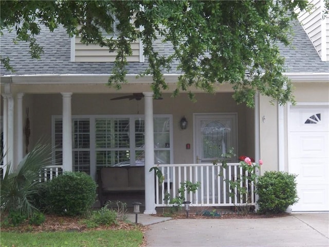 entrance to property featuring roof with shingles, covered porch, a garage, a ceiling fan, and stucco siding