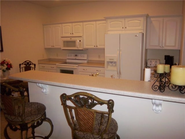 kitchen featuring white appliances, white cabinets, a peninsula, light countertops, and a breakfast bar area