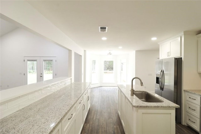 kitchen featuring light stone countertops, sink, french doors, dark wood-type flooring, and an island with sink