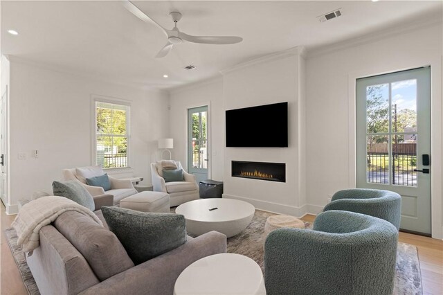 living room featuring light wood-style flooring, a ceiling fan, visible vents, and ornamental molding