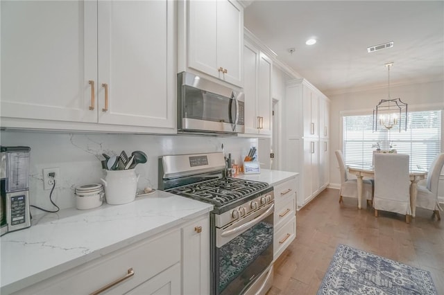 kitchen with light stone countertops, appliances with stainless steel finishes, a notable chandelier, white cabinets, and light hardwood / wood-style floors