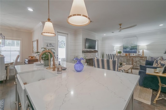 kitchen featuring a center island with sink, decorative light fixtures, light stone counters, and crown molding