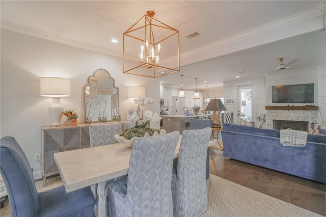 dining area featuring ceiling fan with notable chandelier, wood-type flooring, a fireplace, and ornamental molding