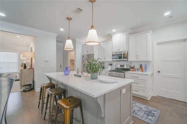 kitchen with appliances with stainless steel finishes, light wood-type flooring, a center island with sink, white cabinets, and hanging light fixtures