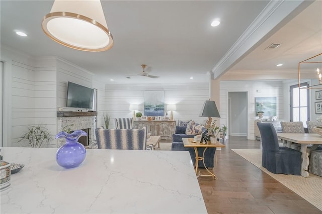 dining room featuring ornamental molding, ceiling fan, a fireplace, dark hardwood / wood-style floors, and wood walls