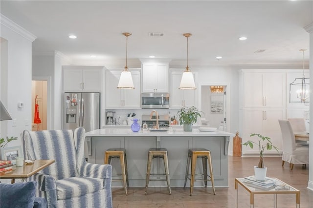 kitchen featuring a kitchen breakfast bar, an island with sink, pendant lighting, white cabinets, and appliances with stainless steel finishes